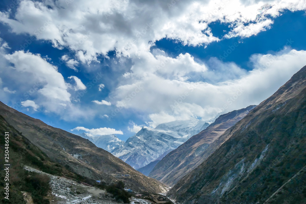 Himalayas, Annapurna Circuit Trek, Himalayas, Nepal.  Endless mountain chains in the back, covered with clouds and snow.  Dry, steep slopes. Freedom, wilderness. Bright sunlight comes through clouds