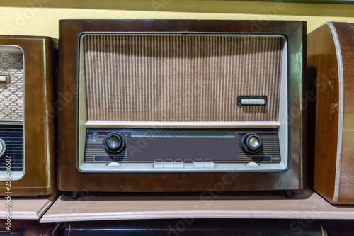 Retro broadcast radio receiver on wooden shelf against yellow background.