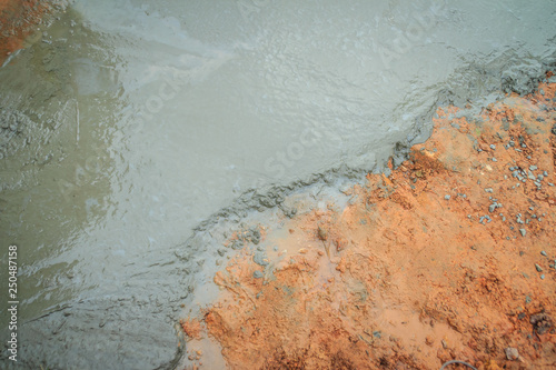 Liquid concrete poured and leveled on the ground. Wet concrete and red soil textured background. Concrete pavement under construction concept.