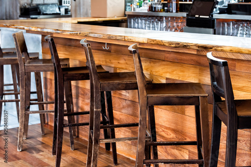 Row of empty wooden vintage bar stools by counter in drink establishment pub during day pattern closeup rustic retro wood and nobody