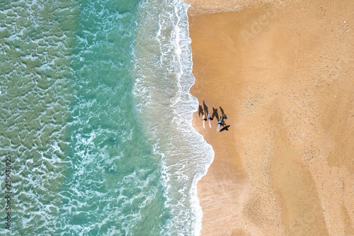 Small group of wave surfers and surf boards standing on a sandy beach in front of The Mediterranean Sea - Top down aerial image.