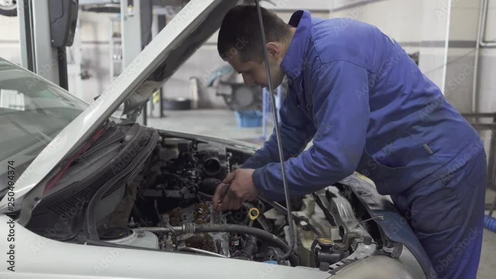 Male young auto specialist tighten the nuts with a wrench in the hood of the car for repairing or making inspection Male young auto specialist tighten the nuts with a wrench in the hood of the car for repairing or making inspection