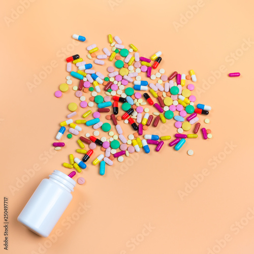 Colored pills, tablets and white bottle on orenge background