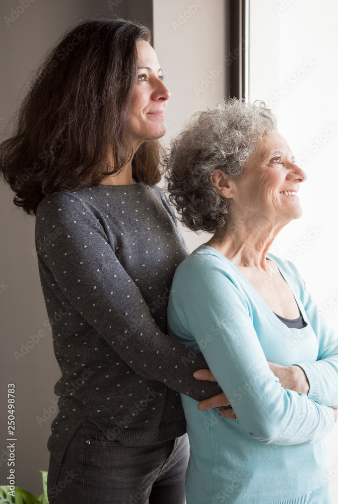 Pensive adult woman embracing mother and standing at window