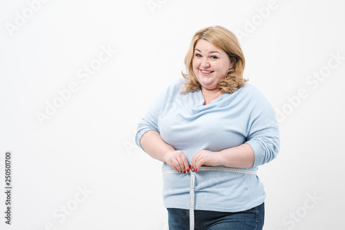 Photos A fat woman measures her waist with a measuring tape in casual clothing on a white background