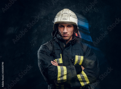 Portrait of a fireman in uniform and helmet stands with crossed arms, looks at the camera with a confident look