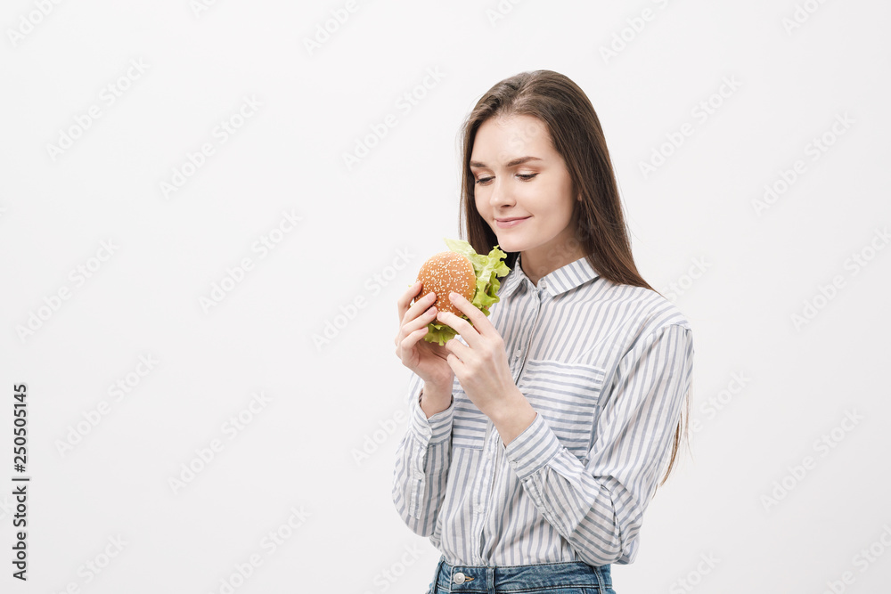 Young beautiful brunette girl on a white background with a hamburger in her hands. Young beautiful brunette girl on a white background with a hamburger in her hands.