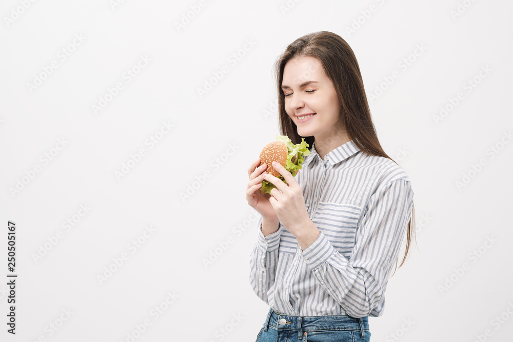Young beautiful brunette girl on a white background with a hamburger in her hands. Young beautiful brunette girl on a white background with a hamburger in her hands.