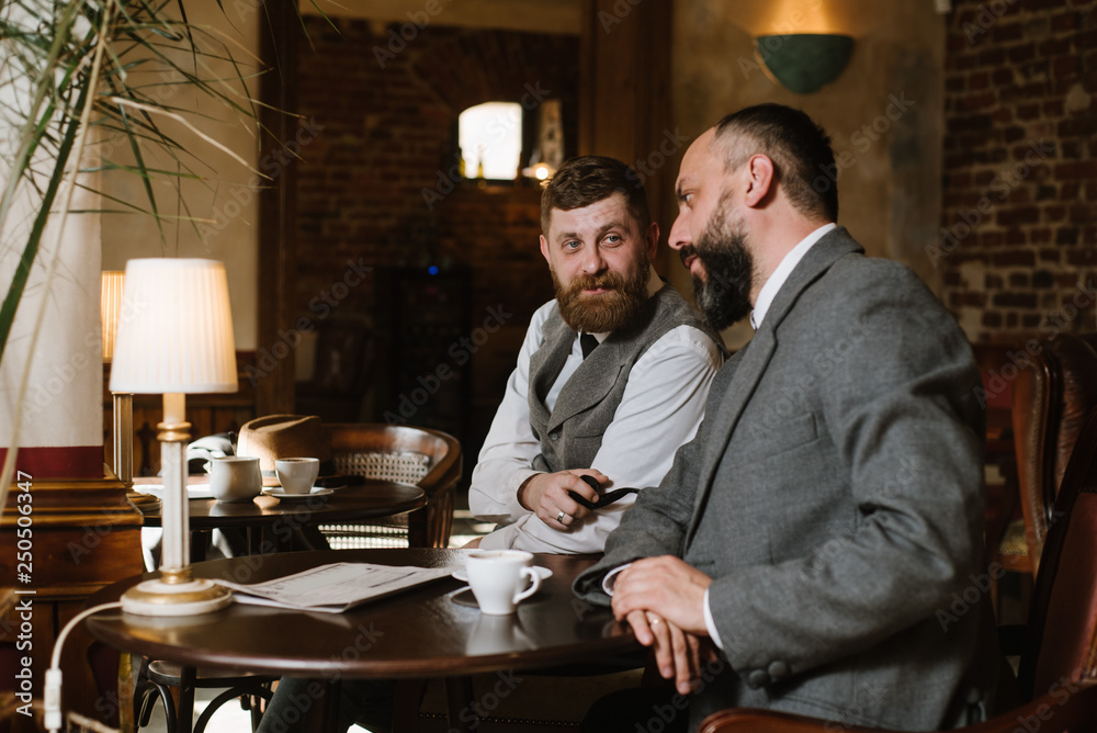 Two bearded men wearing old fashioned suits talking or discuss something in the restaurant Two bearded men wearing old fashioned suits talking or discuss something in the restaurant