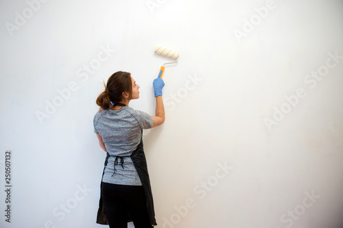 Young brunette woman painting walls with a roller in a new house. Interior design. Renovation. Rear view