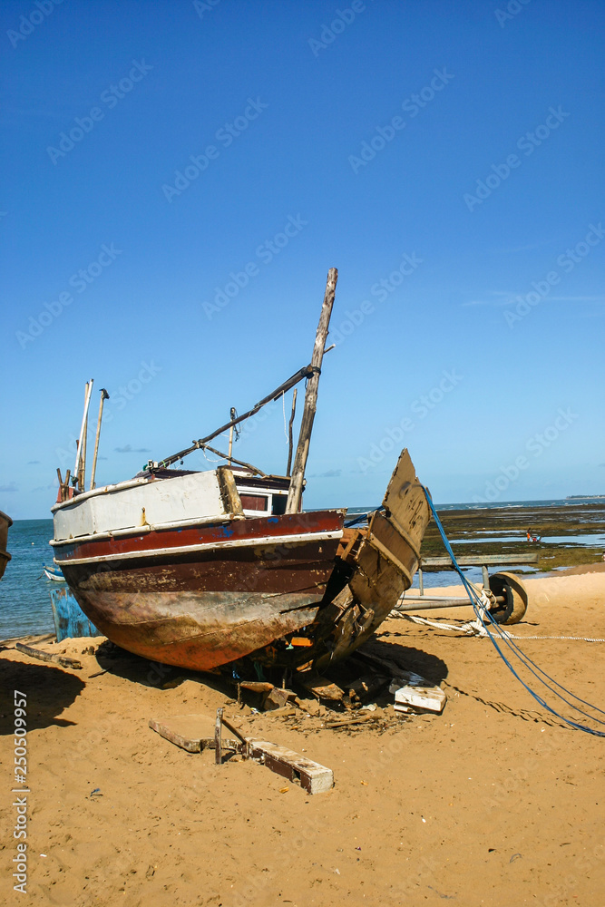 a derelict boat lies in ruins on the beach of a popular fishing location.