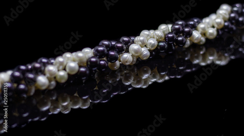 Two mixed strands of natural black pearl beads on a black background with reflection