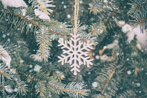 Cute decoration in the form of a wooden snowflake on a Christmas tree, outside next to the house, closeup © rustamank