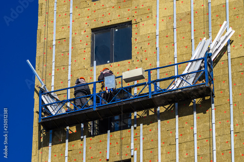 Facing the building with a ventilated facade. Aluminum colored facades. Modern facades of high-rise buildings. Construction of a large residential complex. Suspended construction cradle.