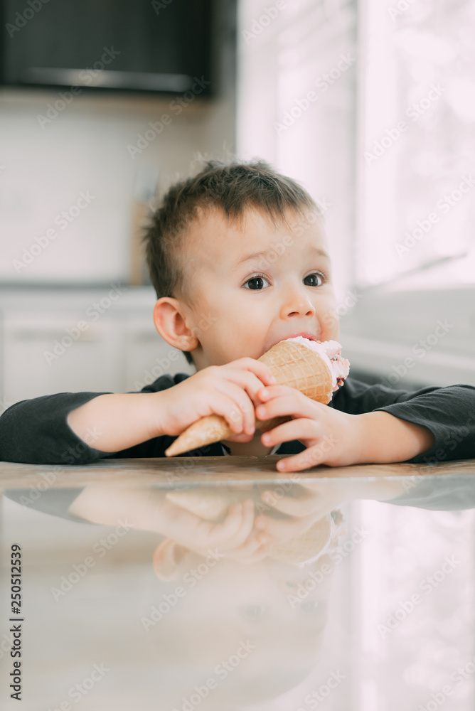 A child in a dark-blue t-shirt in the bright kitchen eating a waffle ice cream cone in the summer house A child in a dark-blue t-shirt in the bright kitchen eating a waffle ice cream cone in the summer house