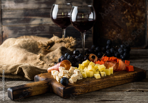 Fototapeta Naklejka Na Ścianę i Meble -  Assorted cheeses on wooden board plate. Camembert cheese, cheese grated bark of oak, hard cheese slices, walnuts, grapes, bread, thyme, top view. Cheese and wine. Antipasto. Red wine