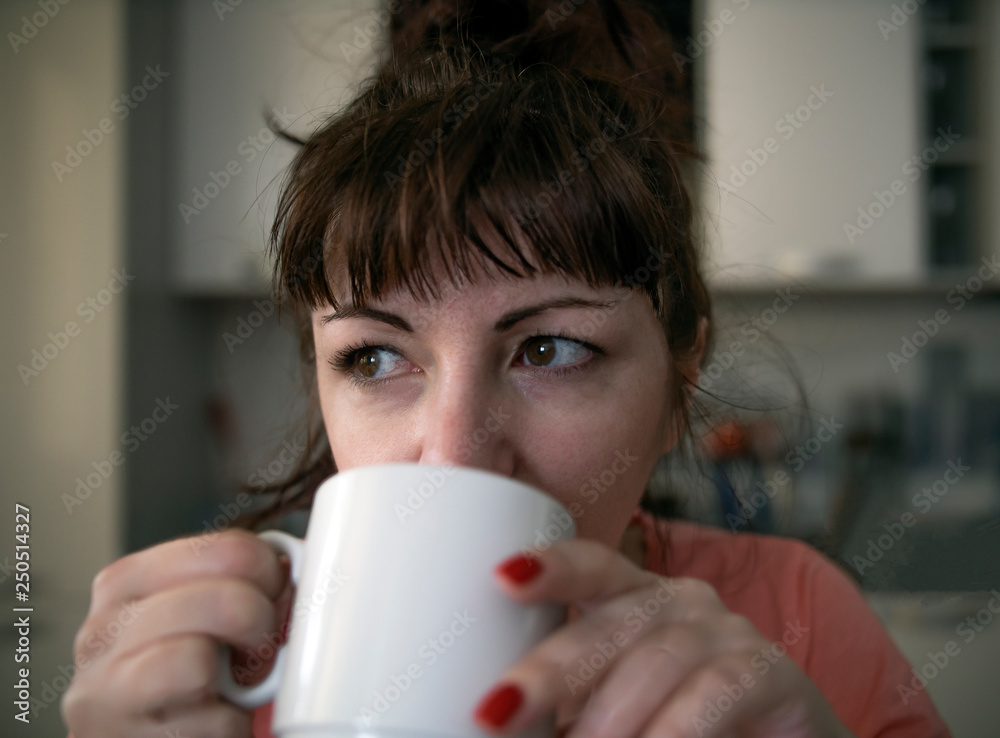Young woman drinking coffee in the morning in the kitchen, tired eyes with red veins Young woman drinking coffee in the morning in the kitchen, tired eyes with red veins