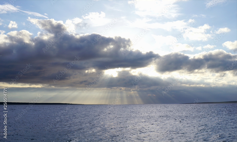 Sun behind cloudy and stormy sky above blue sea surface. Blue nature background