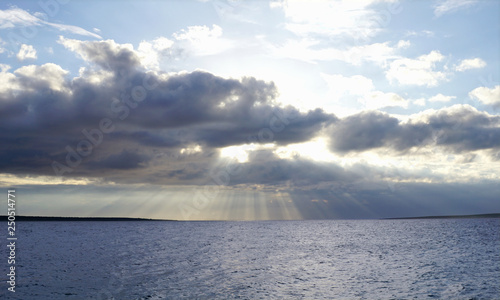 Sun behind cloudy and stormy sky above blue sea surface. Blue nature background