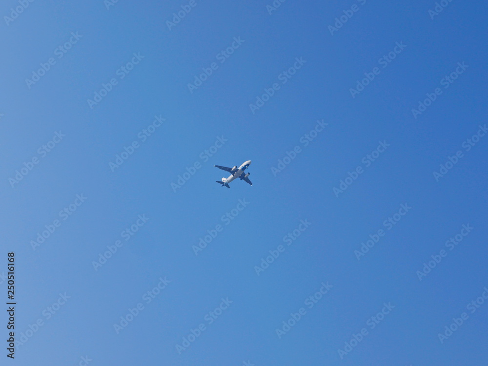 An airplane flying across blue sky, from a far distance, in a sunny day in summer time