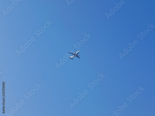 An airplane flying across blue sky, from a far distance, in a sunny day in summer time