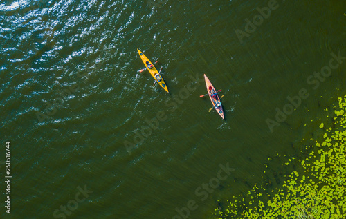 Aerial drone bird's eye view photo of Happy family with two kids enjoying kayak ride on beautiful river. Little boy and teenager girl kayaking on hot summer day. Water sport fun.
