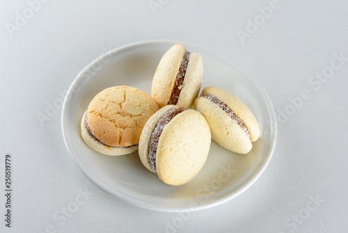 Delicious Argentinian cookies alfajores with cream dulce de leche close-up on the plate. White vanilla macaroons on white background. French delicate dessert for Breakfast in the morning light.