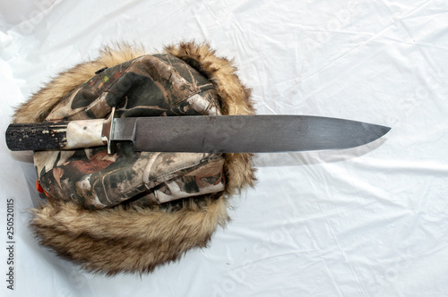 Fotografija A big mountain man bowie knife displayed on a warm furry hat with a white background