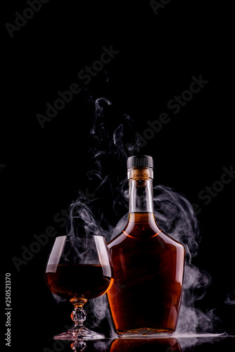 bottle and glass of whiskey or cognac with smoke on dark background