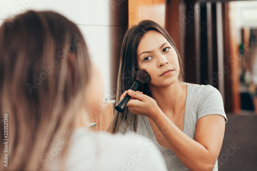 Skin care. Woman applying make-up with brush in front of mirror