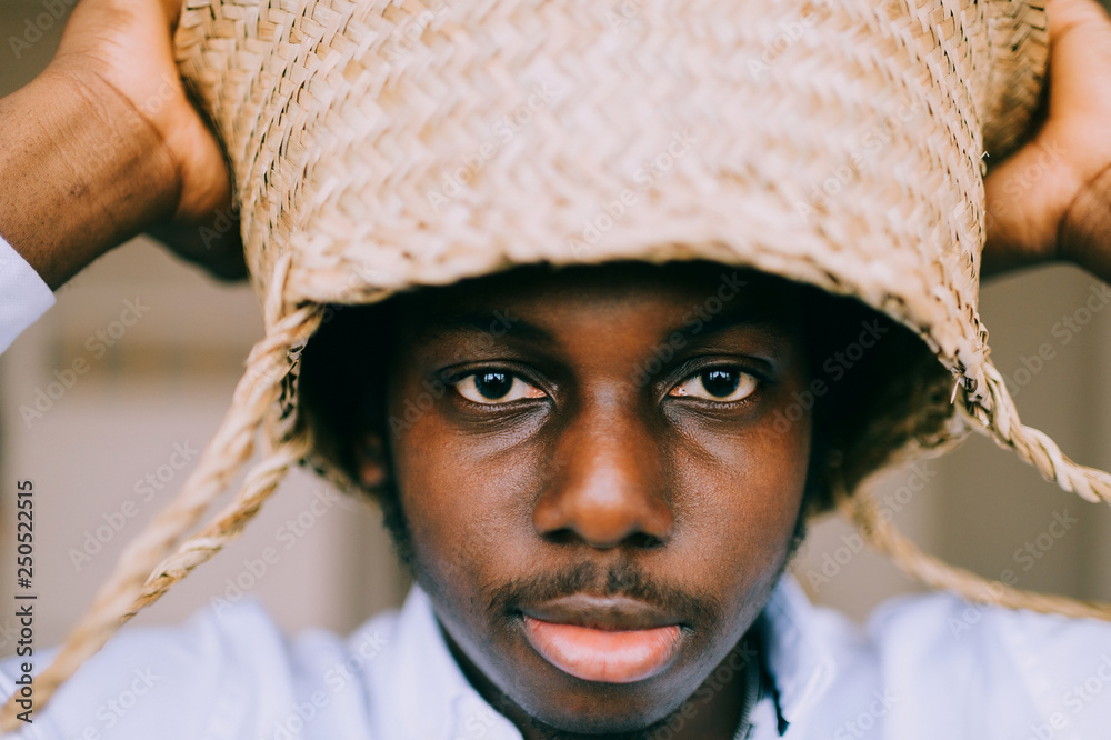 Closeup lifestyle portrait of strange young african black man holding straw  basket above his head on abstract background and looking at camera.  Dark-skinned nigerian boy indoor funny mood portrait. Stock Photo |