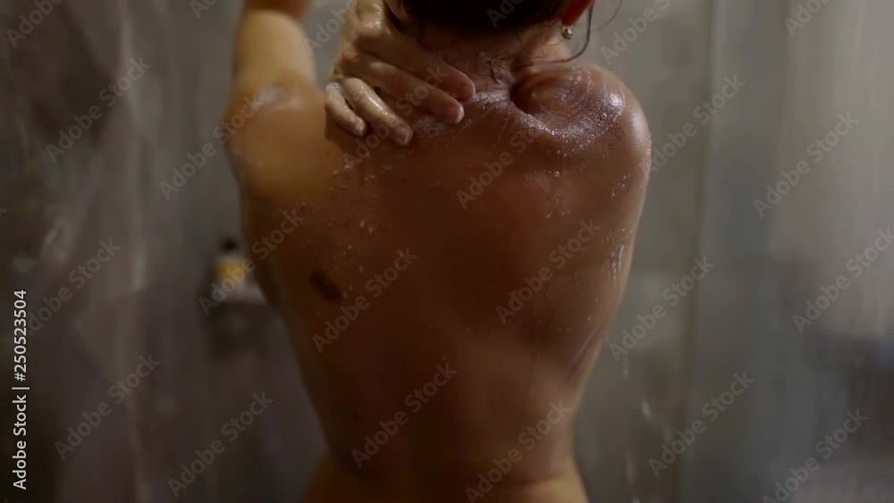 Back view of a beautiful fit naked woman washing her body taking shower. Back view of a beautiful fit naked woman washing her body taking shower.