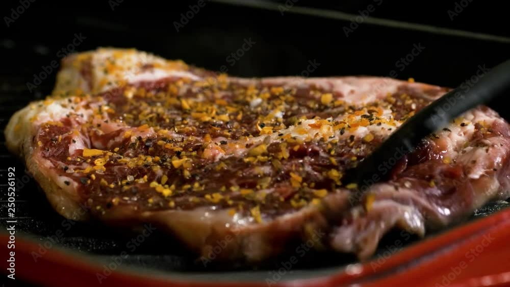 Close Up Shot Of Turning Over The Spiced Steak. The close up clip shows the steak with seasonings turned over to fry the other side. Shot of half cooked steak over a pan.. Close Up Shot Of Turning Over The Spiced Steak. The close up clip shows the steak with seasonings turned over to fry the other side. Shot of half cooked steak over a pan..