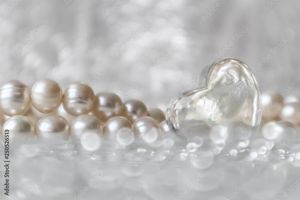 Natural white pearl beads and a transparent heart on a sparkling background Natural white pearl beads and a transparent heart on a sparkling background