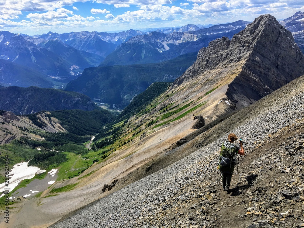 A young hiker exploring the Rocky Mountains on a backcountry hike along the spectacular Northover Ridge trail in Kananaskis, Alberta, Canada.  A beautiful valley is far below.