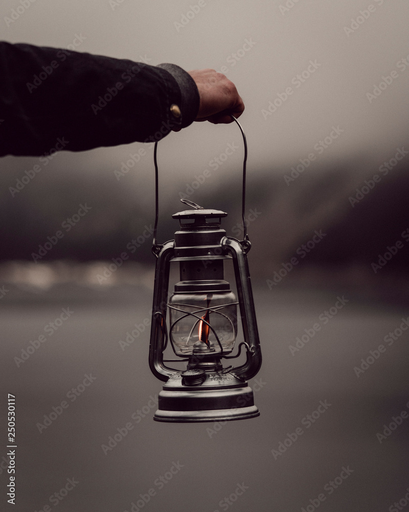 Man's hand holding lantern by lake Photos | Adobe Stock