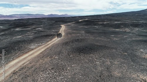 Aerial scene of 4x4 expedition van driving off road between beds of lava, black lapillis, Dark desertic region. Colorfull mountains at background. Mistic barren landscape. Catamarca, Argentina  photo