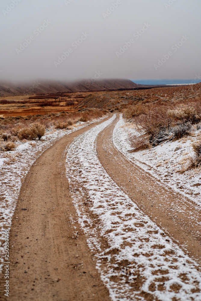 tire tracks in snow on brown desert road in Eastern Sierra Nevada mountain valley winter landscape in California