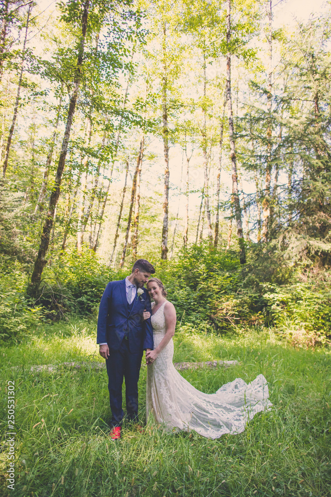 Newlywed couple standing on grassy field against trees in forest Newlywed couple standing on grassy field against trees in forest