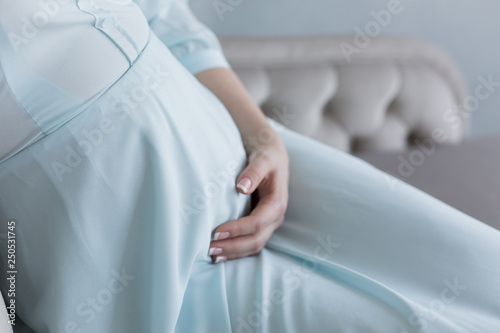 the pregnant woman keeps her hands on her stomach. pregnant in blue dress. pregnant belly