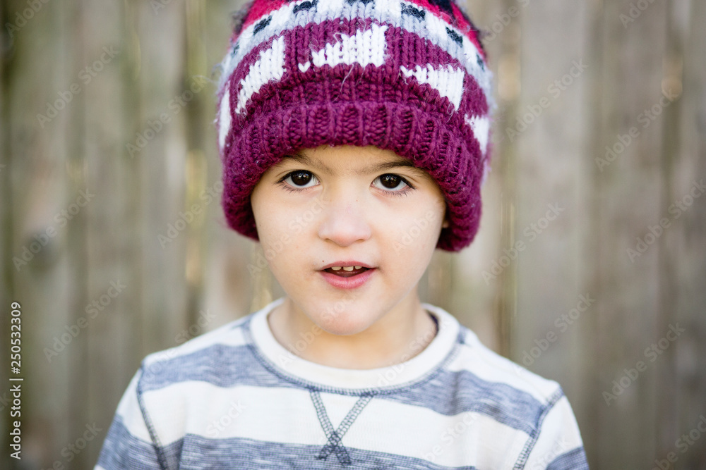 Close-up portrait of cute boy wearing knit hat while standing against fence in yard Close-up portrait of cute boy wearing knit hat while standing against fence in yard