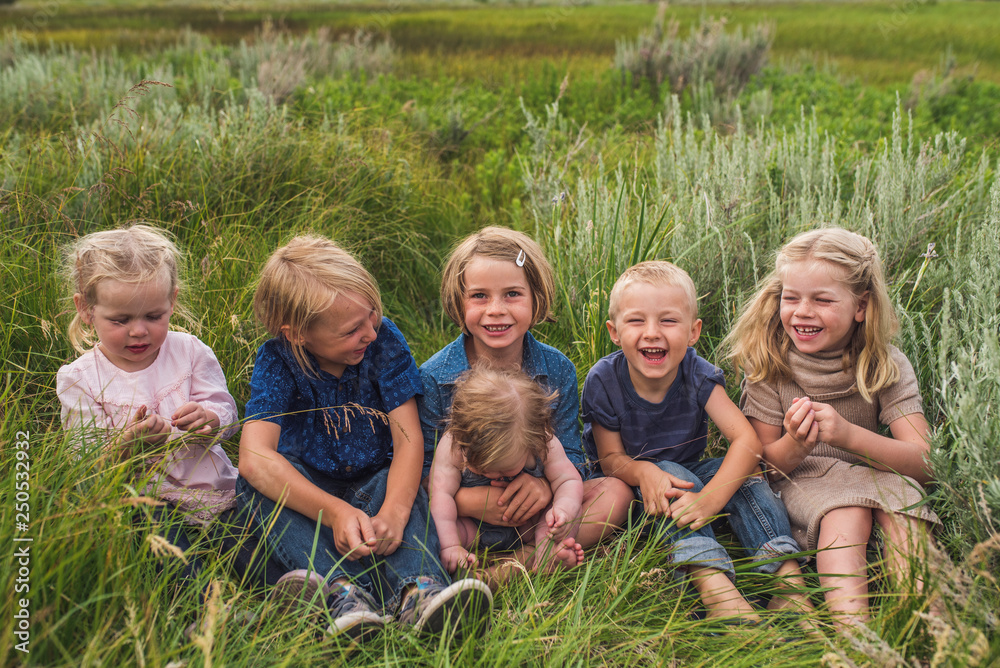 Cute happy friends sitting together on field by plants Cute happy friends sitting together on field by plants