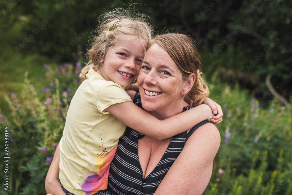 Portrait of happy mother carrying daughter while standing on grassy field in forest Portrait of happy mother carrying daughter while standing on grassy field in forest