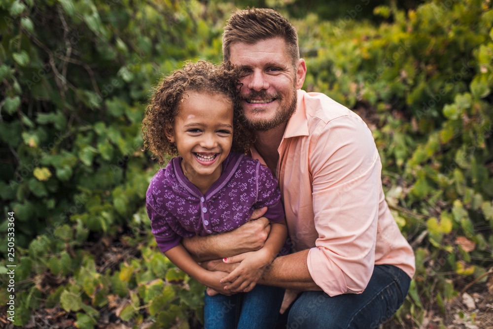 Portrait of father embracing happy daughter while kneeling against plants in park Portrait of father embracing happy daughter while kneeling against plants in park