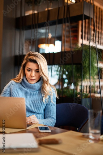 Young casual businesswoman working on laptop in a cafe.