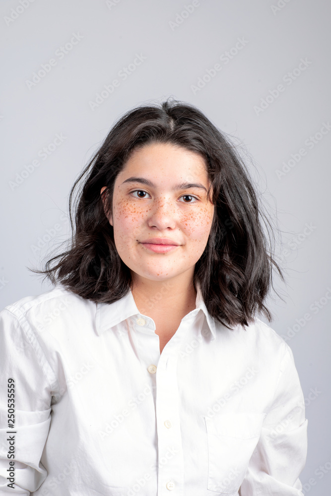 Portrait of smiling teenage girl sitting against gray background Portrait of smiling teenage girl sitting against gray background