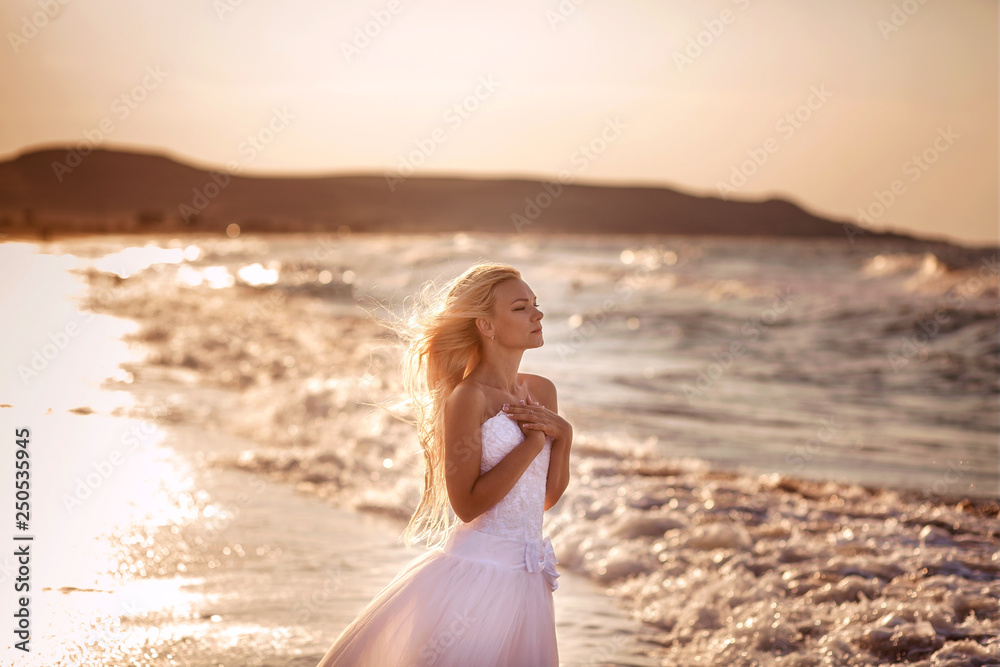 beautiful bride in white dress at sunset on the ocean or sea on an exotic island by the water. Sunny horizon. Wedding, honeymoon concept. Young woman resting on vacation in nature