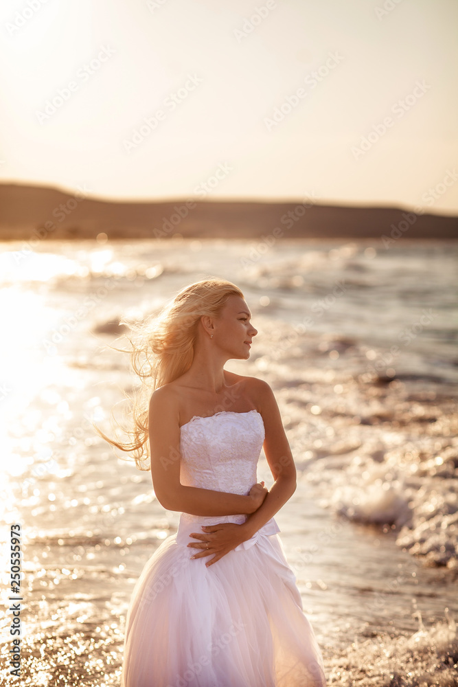 beautiful bride in white dress at sunset on the ocean or sea on an exotic island by the water. Sunny horizon. Wedding, honeymoon concept. Young woman resting on vacation in nature beautiful bride in white dress at sunset on the ocean or sea on an exotic island by the water. Sunny horizon. Wedding, honeymoon concept. Young woman resting on vacation in nature