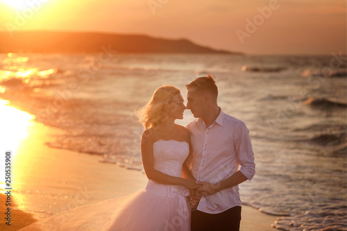 happy beautiful young couple in wedding dress and suit by the sea at sunset, waves 