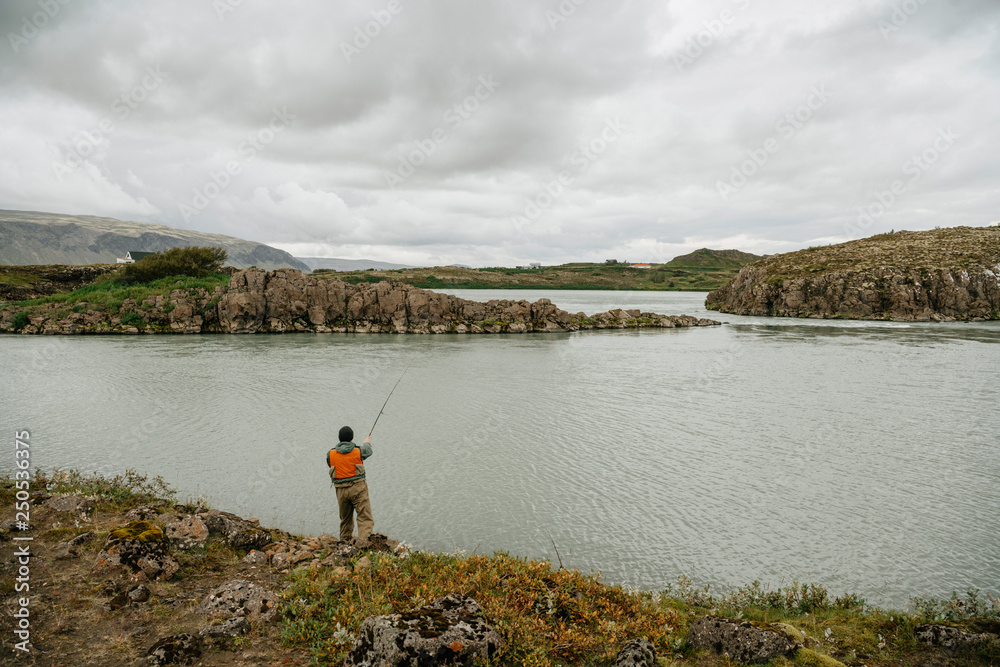 Rear view of man fishing in lake against cloudscape at Iceland Rear view of man fishing in lake against cloudscape at Iceland